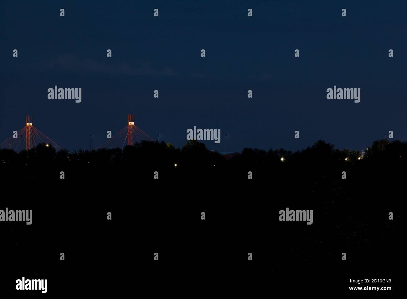 Eine dunkle Vorstadtlandschaft bei Dämmerung, mit zwei beleuchteten roten Strukturen und Straßenlaternen, die durch die Bäume glitzern. Stockfoto