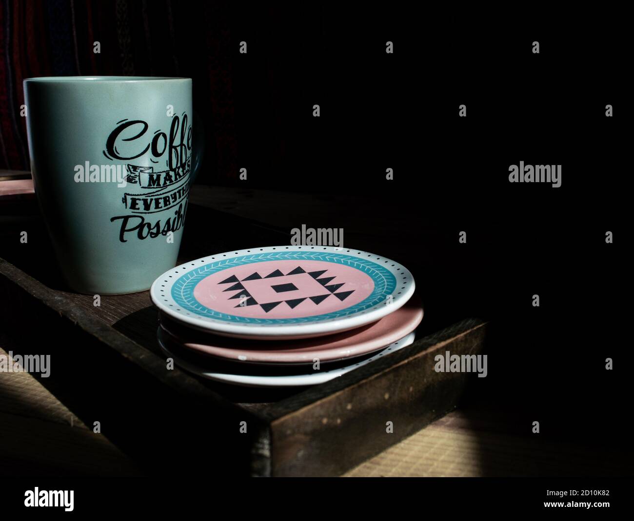 Nahaufnahme eines olivgrünen Kaffeetassen mit Texten Und bunte kleine Teller im Schatten Stockfoto