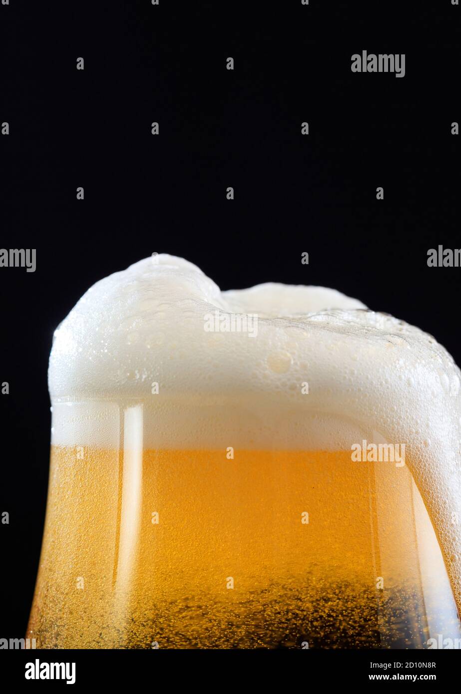 Bierschaum-Detail auf schwarzem Hintergrund, schaumig überlaufendes Glas goldenes Ale Bier, Nahaufnahme beschnittene Porträt-Ansicht, Kopierraum Stockfoto