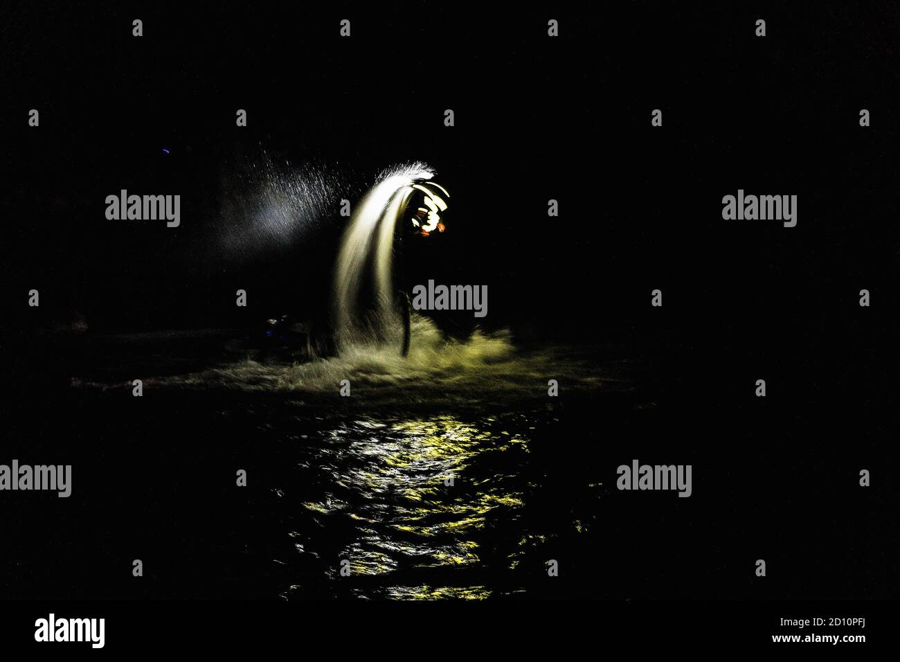 Flyboarding bei Nacht in einem Steinbruch in der Tschechischen Republik. Ein nicht identifizierter Mann führt nachts das Flyboarding durch. Bewegungseffekt, Langzeitbelichtung. Stockfoto