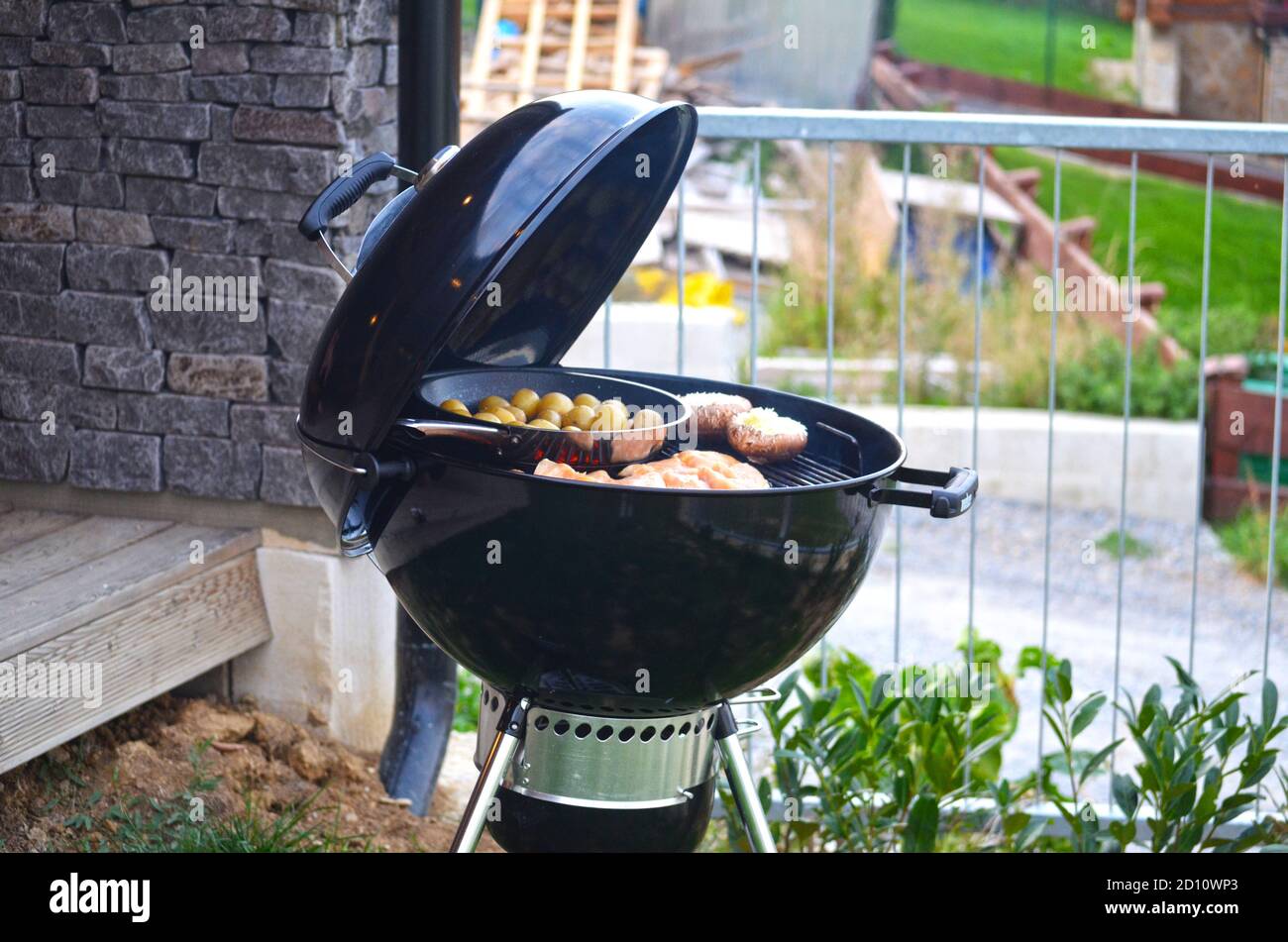 Schwarz geöffneter Grill mit Lebensmitteln. Fleisch, Kartoffeln, Waldpilze. Grill. Stockfoto