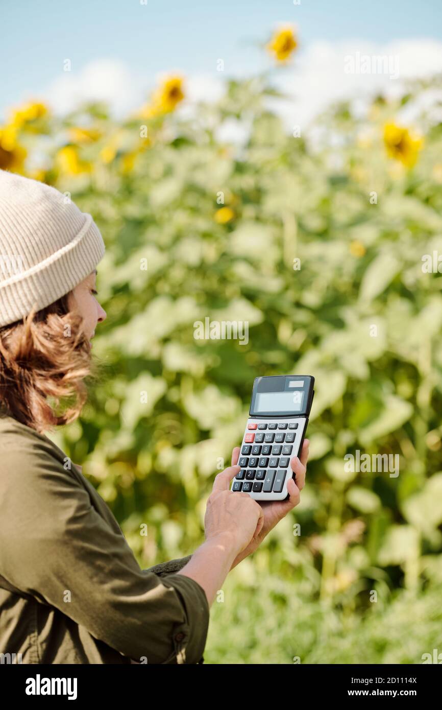 Reife weibliche Landwirt in Arbeitskleidung halten Taschenrechner und schieben seine Tasten Stockfoto