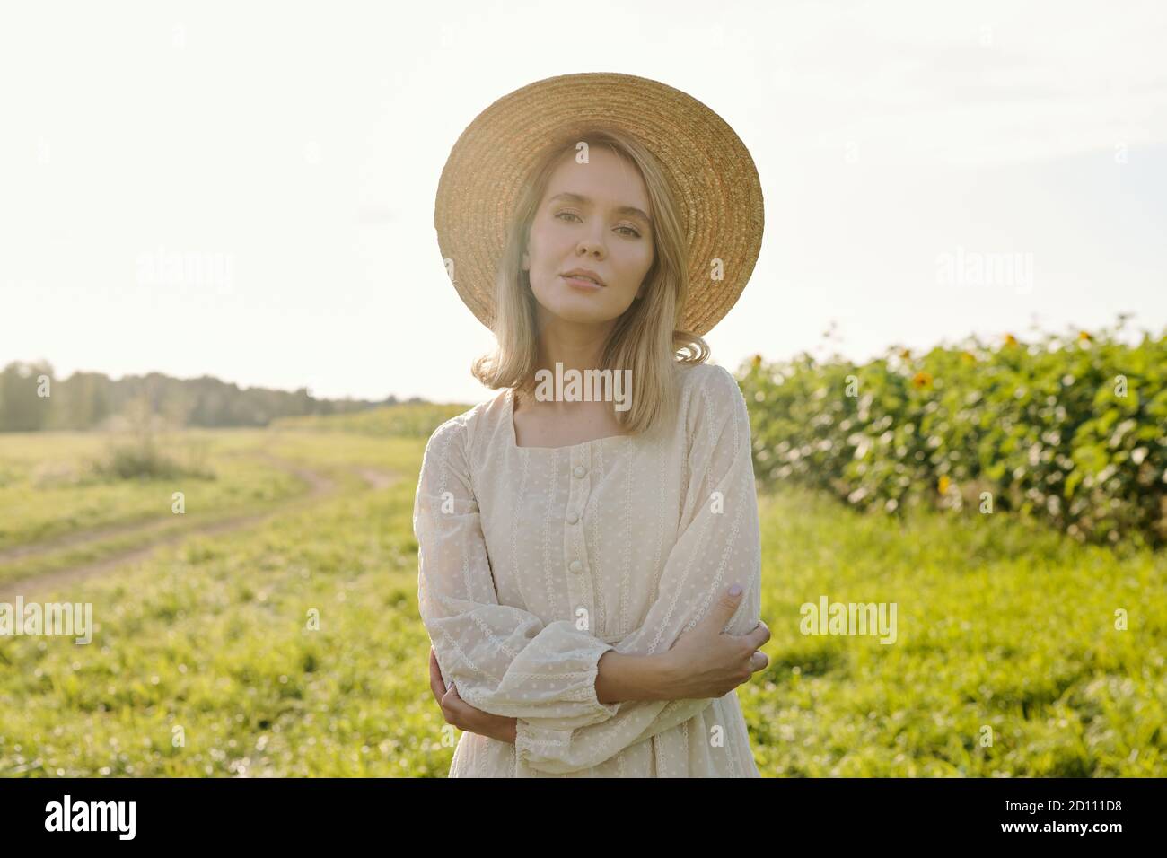 Wunderschöne junge blonde Frau in Strohhut und weißen Land Modisches Kleid Stockfoto