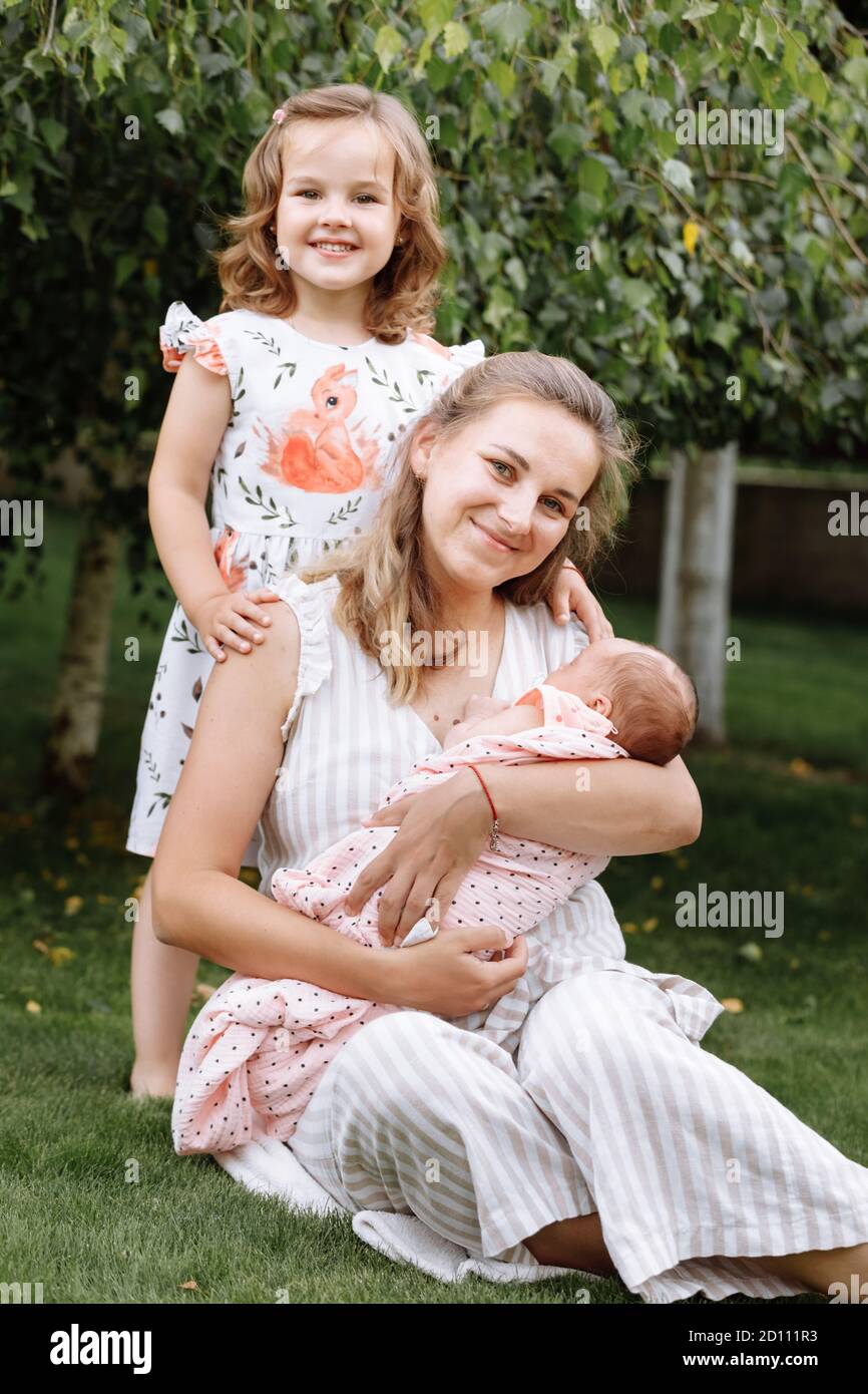 Portrait von liebevoller Mutter und zwei entzückende Kinder. Kleines Mädchen und neugeborenes Mädchen mit Mutter im Freien am Sommertag. Glückliche Familie verbrachte Zeit zusammen Stockfoto