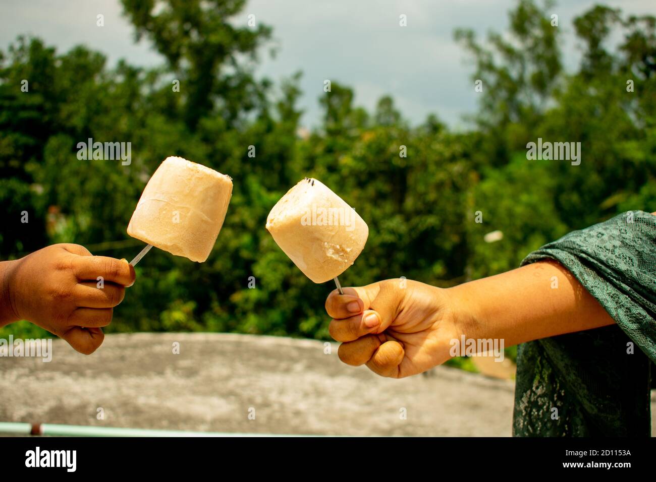 Kinder halten hausgemachtes Eis von der Hand in einem Grüne Umgebung unter wolkenblauem Himmel an einem Sommertag Natürlicher Hintergrund Stockfoto