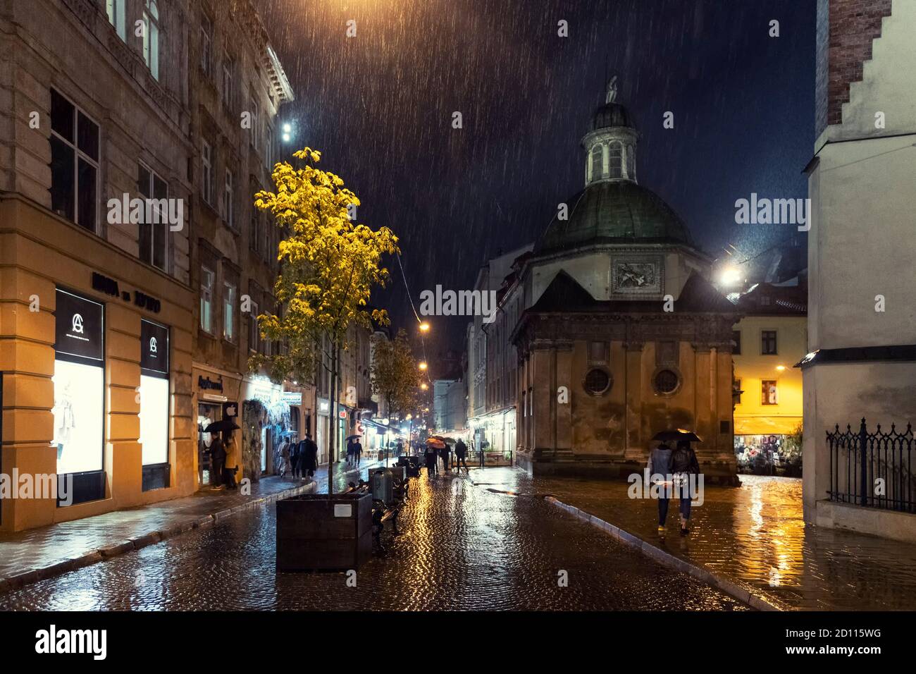 2020-09-29 Lviv, Ukraine. Herbstregen in Lviv. Nachtszene in der Altstadt von Lviv. Fußgänger auf nassem Kopfsteinpflaster mit Lichtreflexen der Stadt Stockfoto