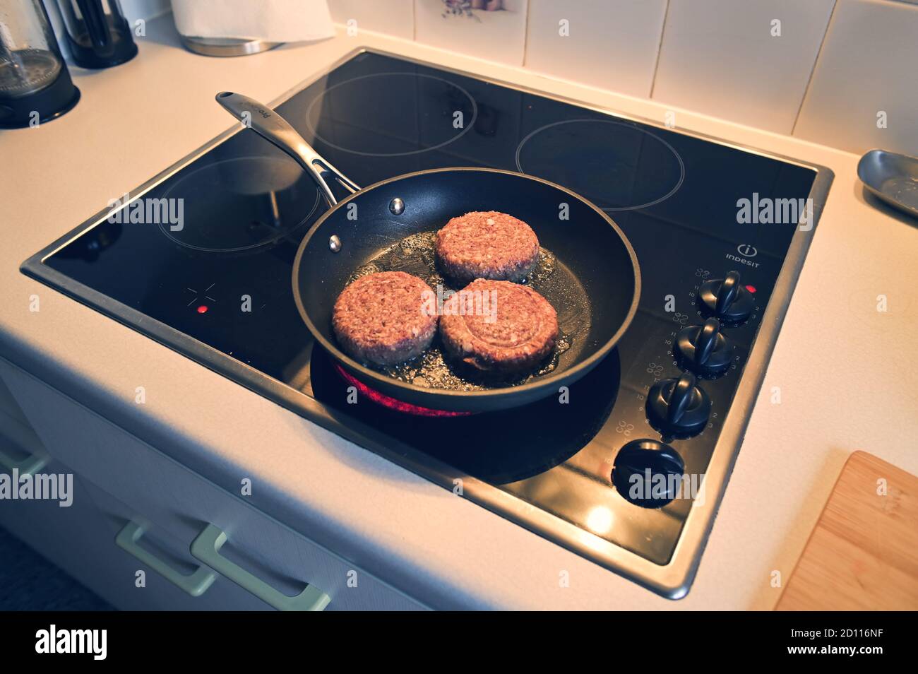 Seitenwinkel von drei Beefburgern, die in einer Bratpfanne kochen Auf einem Herd Stockfoto