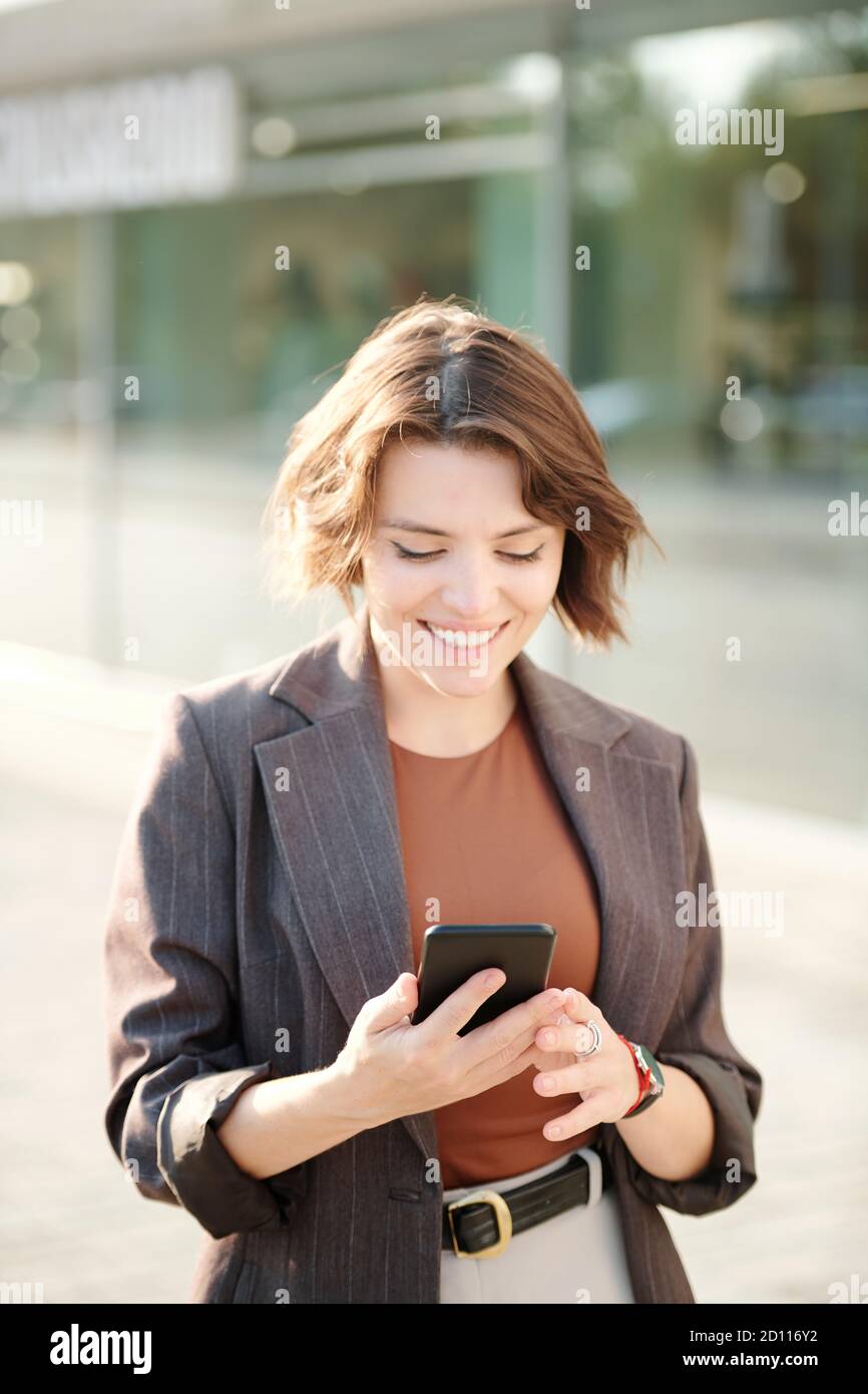 Fröhliche junge Geschäftsfrau in Smart Casualwear Scrollen durch Kontakte Stockfoto