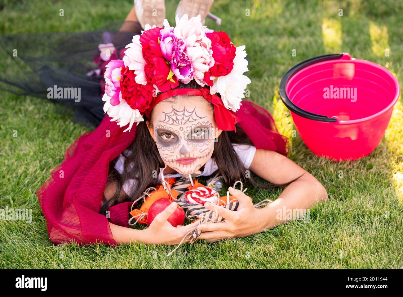 Nettes Mädchen mit bemalten Gesicht hält Haufen von süßen halloween Leckereien auf grünem Rasen Stockfoto