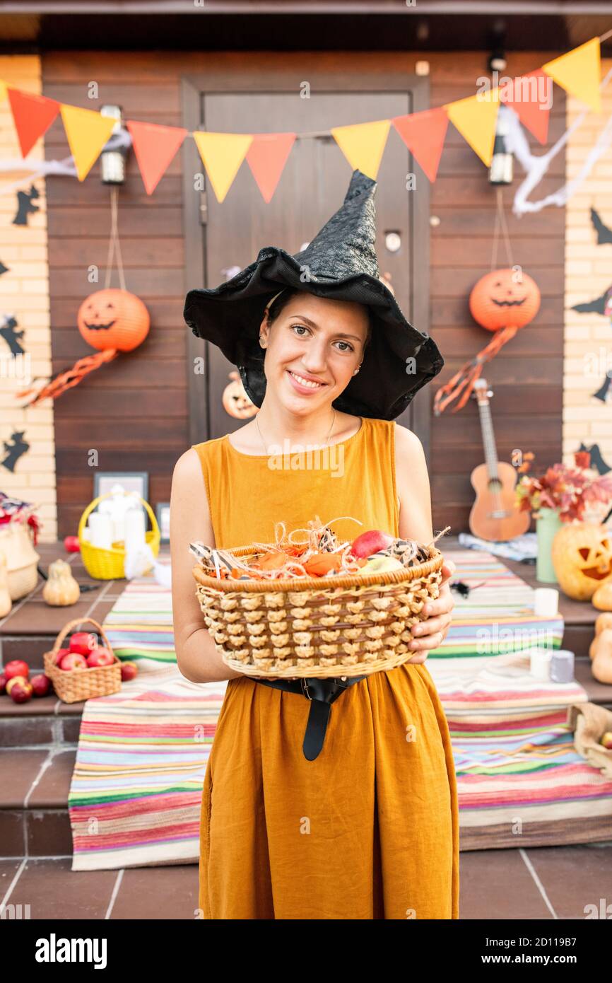 Junge fröhliche hübsche Frau in schwarzem Hut von halloween Hexe Leckereien halten Stockfoto