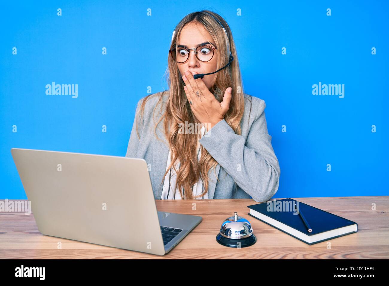 Junge schöne blonde Frau trägt Operator-Headset im Callcenter Büro Abdeckung Mund mit Hand, schockiert und Angst vor Fehler. Überrascht ex Stockfoto