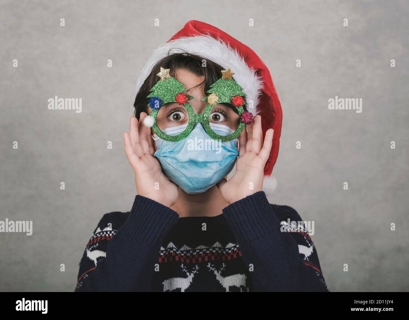 Frohe Weihnachten, Lustiges Kind mit medizinischer Maske und lustige weihnachtsgläser auf grauem Hintergrund Stockfoto