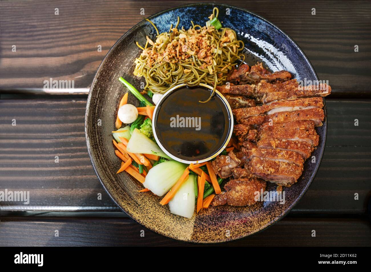 Asiatisches Gericht mit gebratener Ente, Gemüse, Nudeln und Teriyaki-Sauce in einer flachen Schüssel auf einem Holztisch, Blick von oben, ausgewählter Fokus Stockfoto