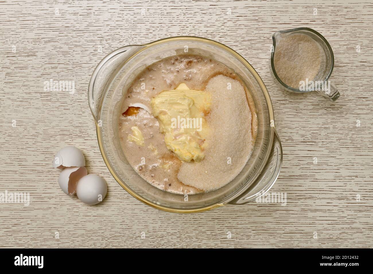 Das Stadium der Zugabe von Zucker zu einer Mischung aus Milch, Eier und Hefe, in einem Glas-Topf. Daneben ist ein Krug und eine Schale. Stockfoto