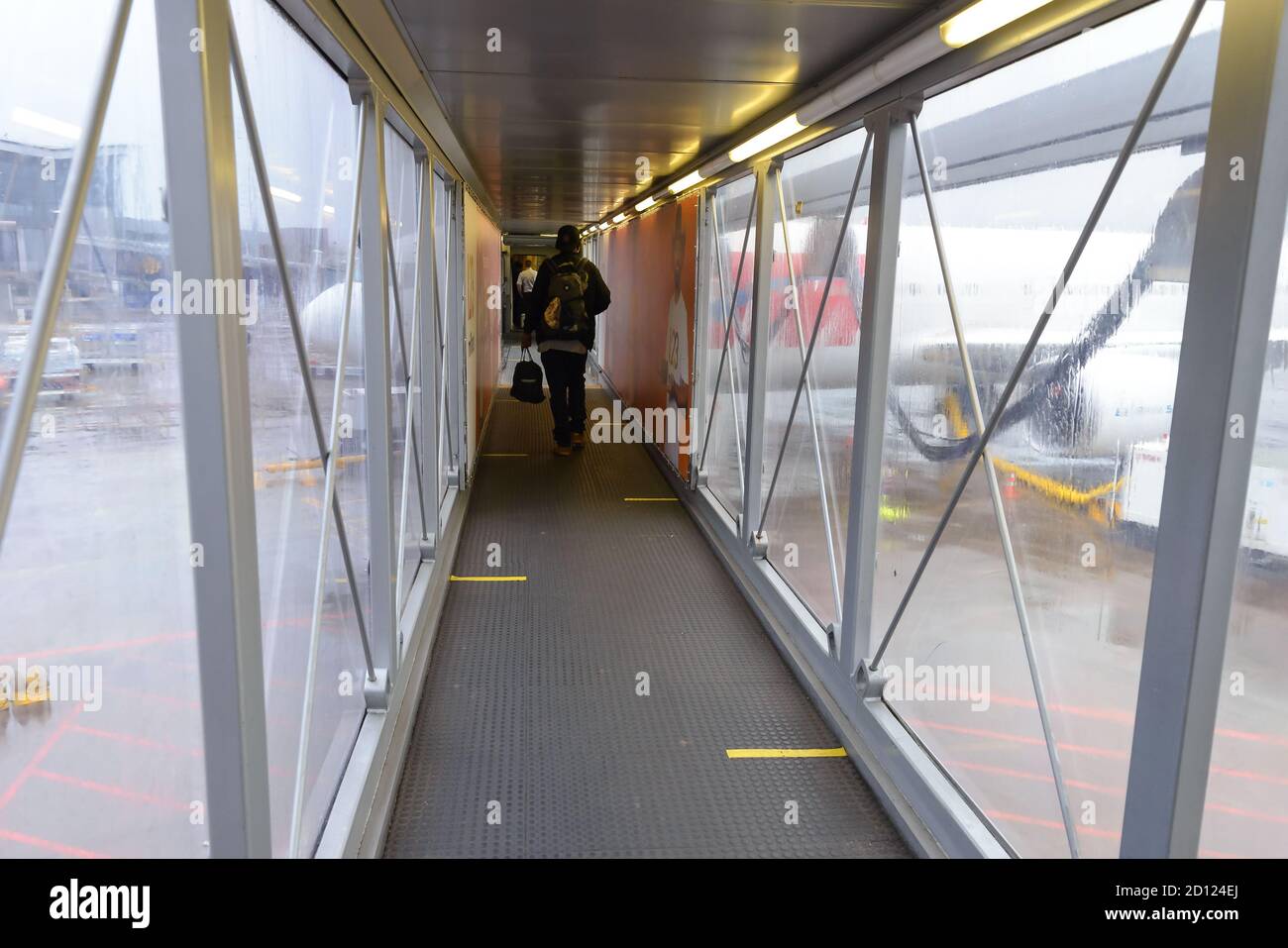 Passagiere an Bord der Brücke (Jet-Brücke) mit Bodenmarkierungen für soziale Distanzierung aufgrund von Coronavirus / Covid 19 Pandemie. Jetway mit Bodenmarkierungen. Stockfoto
