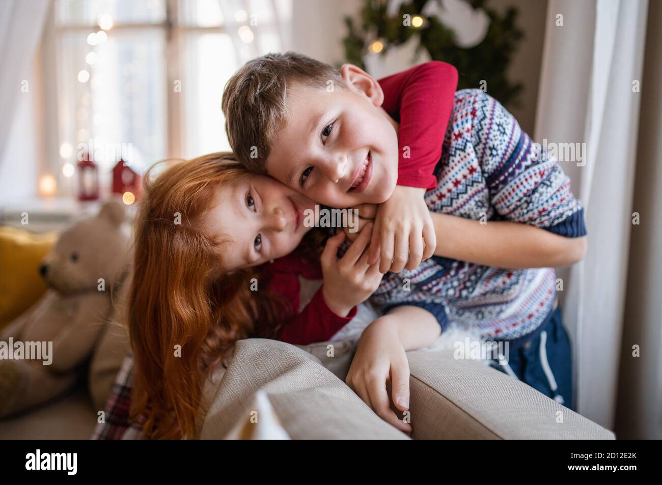 Kleine Mädchen und Jungen drinnen zu Hause zu Weihnachten, Blick auf die Kamera. Stockfoto