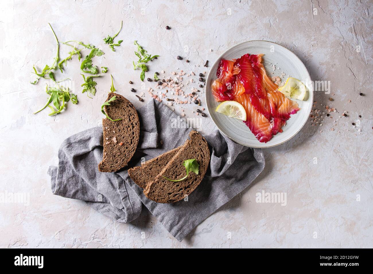 In Scheiben geschnittene rote Beete marinierter Lachs für Sandwiches mit in Scheiben geschnittenen Roggenbrot, rosa Salz, Pfeffer, grünen und Zitrone in Blue Platten mit textilen Serviette o serviert. Stockfoto