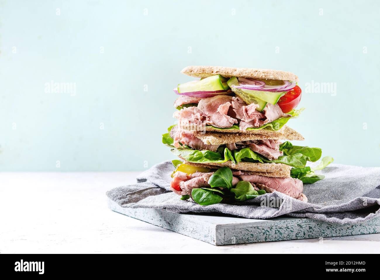 Rindfleisch und Gemüse Sandwiches mit in Scheiben geschnittenen Fleisch, Gurken, grüner Salat, Roggen Vollkornbrot im Stapel auf Holz Tablett mit Textilien Serviette über Graues gre Stockfoto