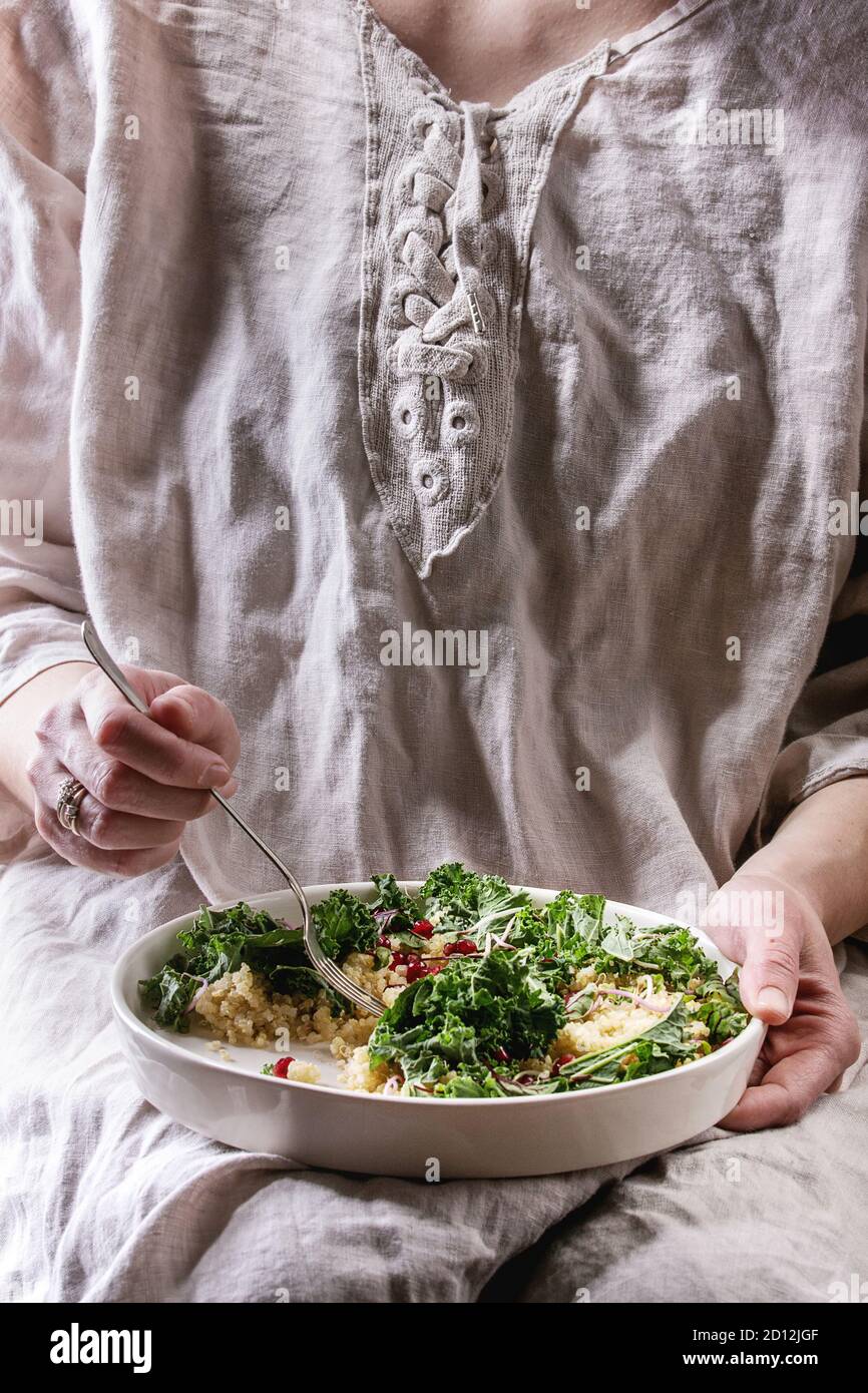 Sitzung Frau halten und Essen vegan Quinoa Salat mit Grünkohl, junge Rote Bete Blätter, Granat Samen, in Scheiben geschnittenen Avocado in weiße Platte. Gesunde Ernährung Stockfoto