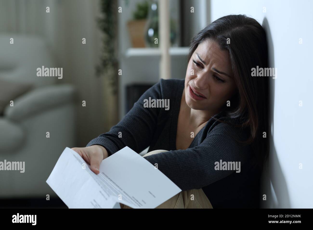 Traurige Frau, die sich beschwerte, nachdem sie einen Brief auf dem gelesen hatte Etage allein zu Hause in der Nacht Stockfoto