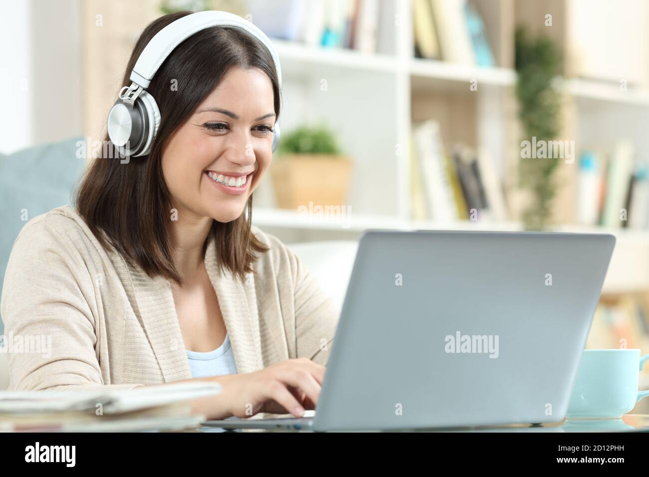 Glückliche Frau mit Kopfhörern mit einem Laptop sitzen in einem Schreibtisch zu Hause Stockfoto