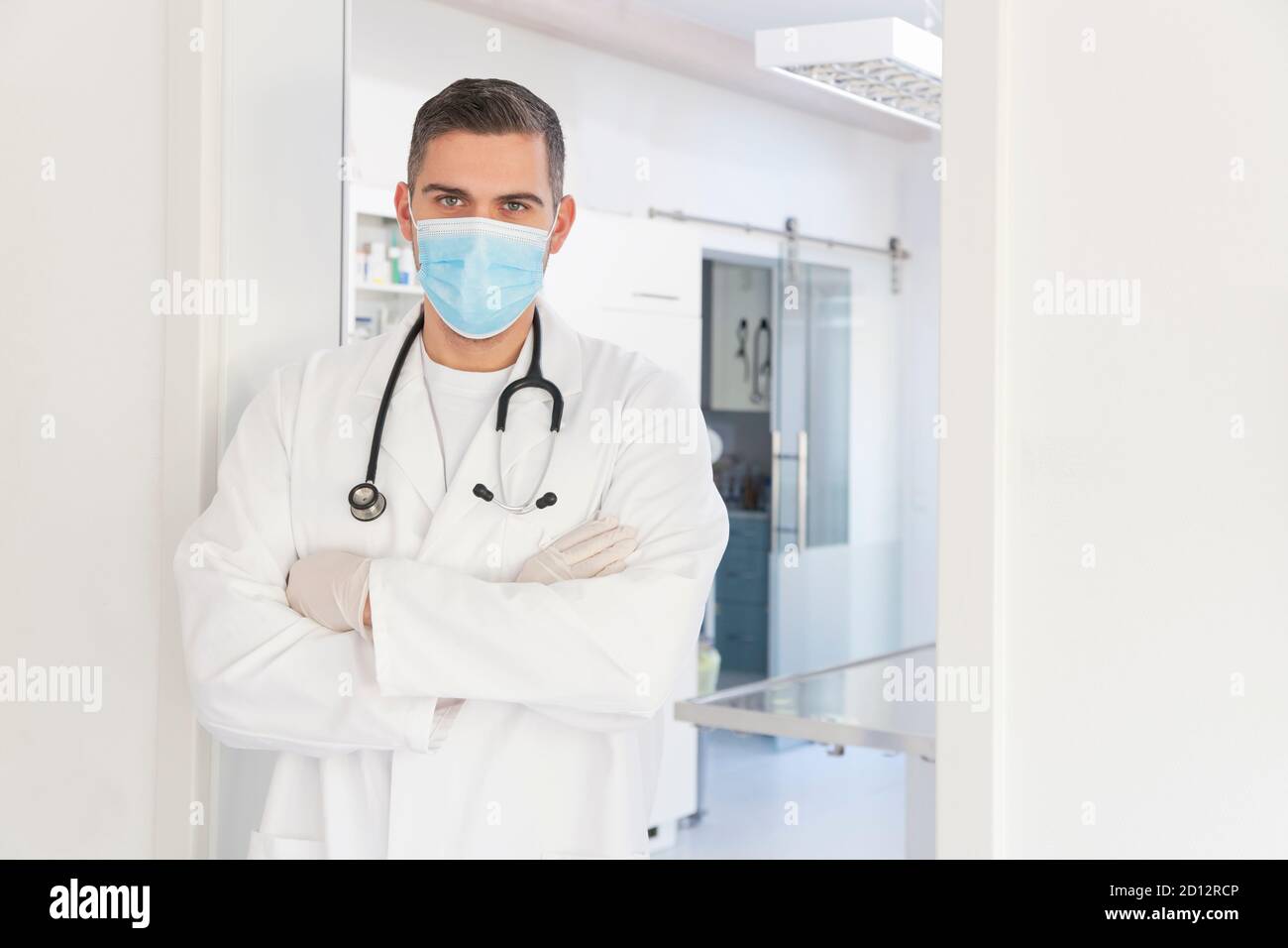 Junger selbstbewusster Arzt oder Chirurg mit medizinischer Maske im Stehen Vorderseite einer Operation im verschwommenen Hintergrund Stockfoto