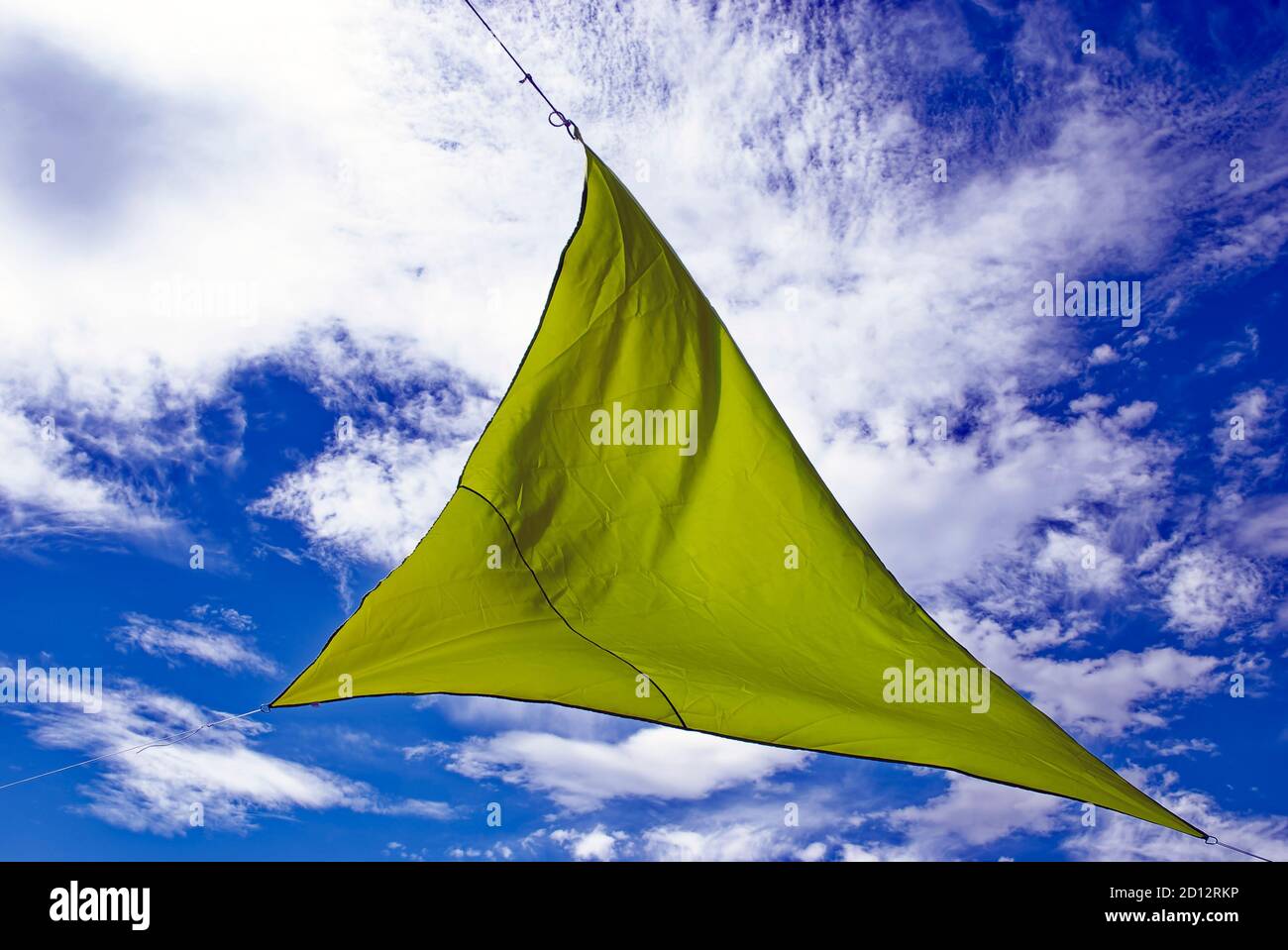 Grünes Segel gegen den Himmel - ein dreieckiges grünes Segel Gegen einen leicht bewölkten blauen Himmel Stockfoto