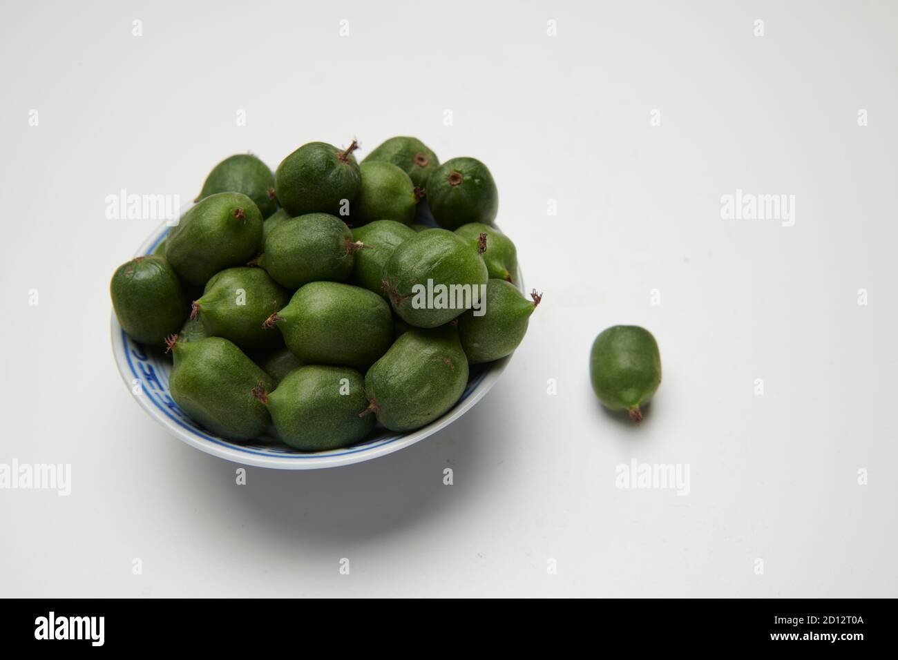 Kiwi-Beeren (Actinidia arguta) in einer kleinen weißen Schüssel auf einer weißen Arbeitsplatte. Stockfoto