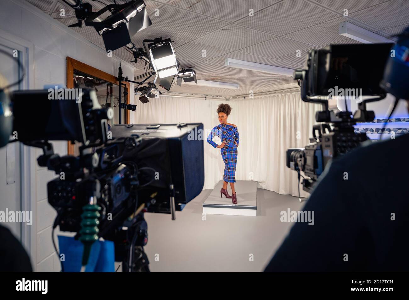 Eine Fernsehsendung, die in einem Studio gedreht wird. Eine Frau modelliert ein Kleid während des Fashion-Segments. Es wird zwischen zwei Filmkameras gedreht. Stockfoto