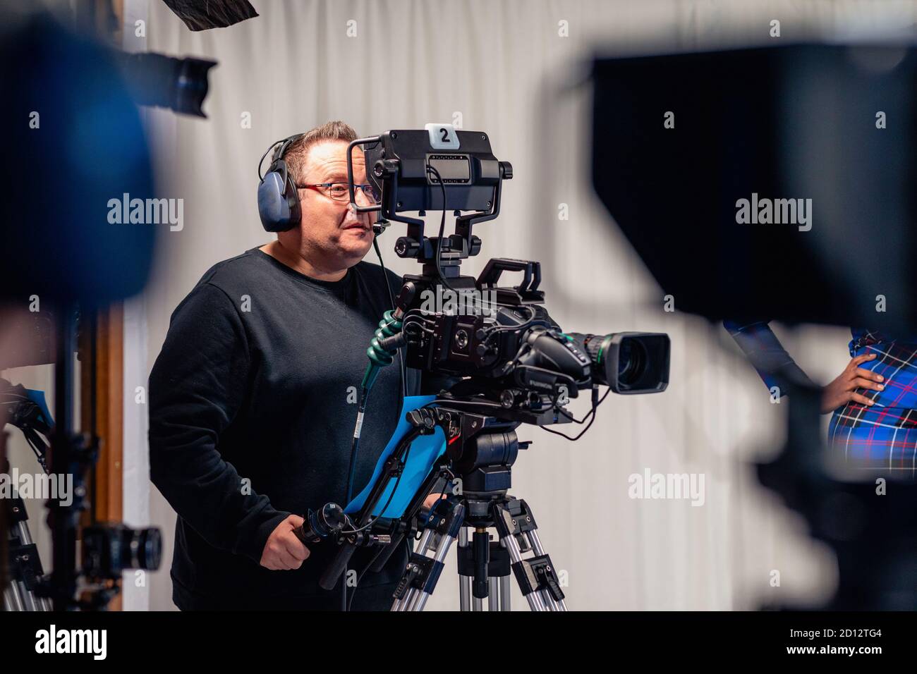 Ein Kameramann, der ein Headset trägt und beim Filmen einer Fernsehsendung durch den Sucher der Filmkamera schaut. Stockfoto