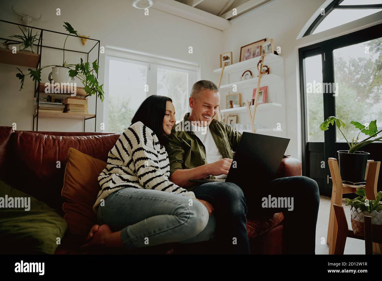 Junges Paar sitzt auf der Couch und schaut auf einen Laptop - 2 Personen Streaming von ihrem Laptop Stockfoto