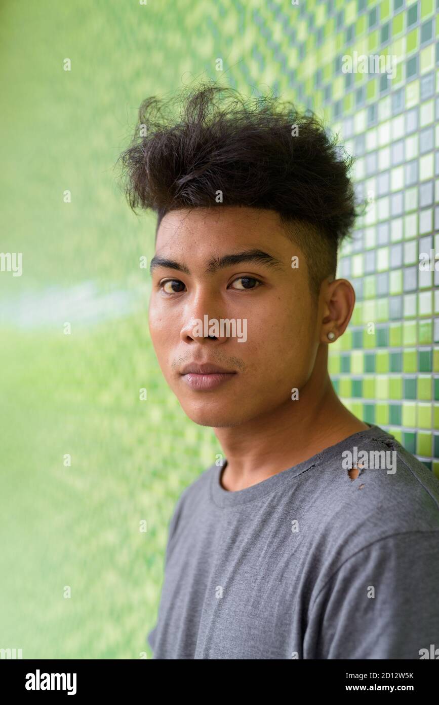 Gesicht des jungen asiatischen Mannes mit lockigen Haaren gegen grün Wand im Freien Stockfoto