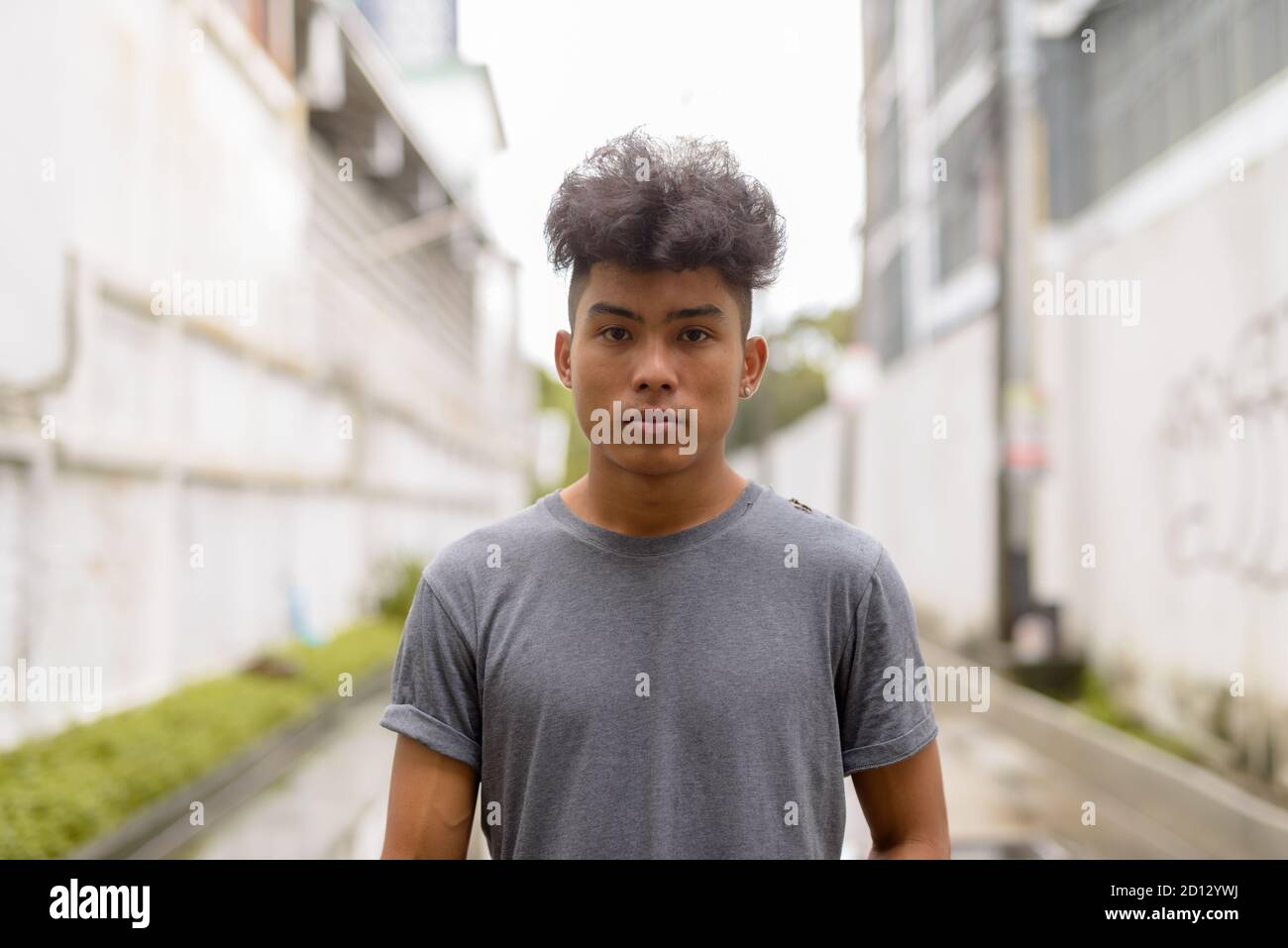 Junger asiatischer Mann mit lockigen Haaren in den Straßen im Freien Stockfoto