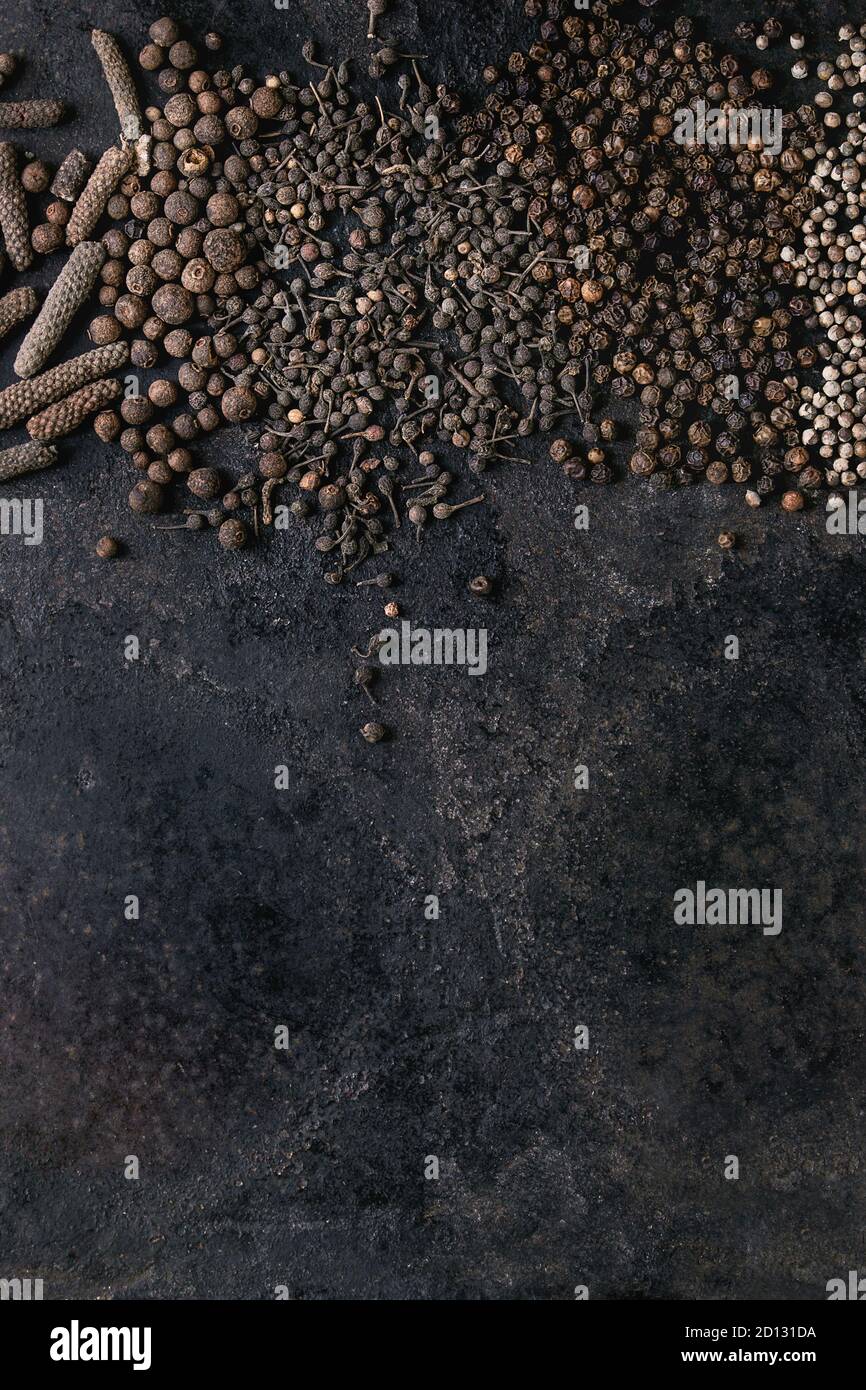 Vielfalt an verschiedenen schwarzen Paprika Allspice, Pimento, langer Pfeffer, Mönche Pfeffer, Pfefferkörner über alten schwarzen Eisen Textur Oberfläche. Hintergrund für das Essen. Oben Stockfoto