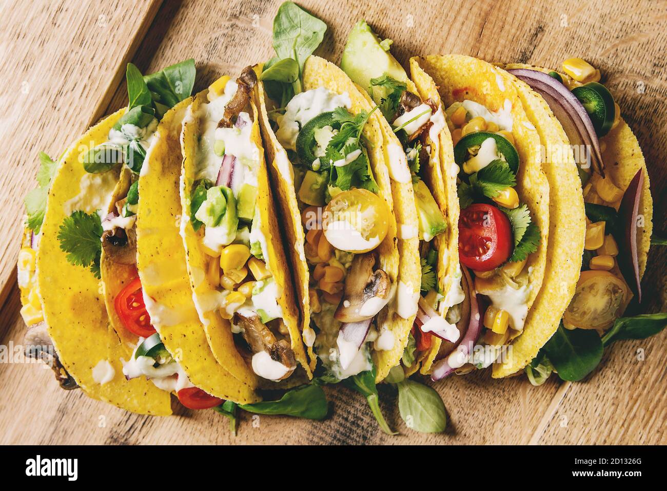 Auswahl an vegetarischen Mais Tacos mit Gemüse, grüner Salat, Chili auf Holzplatte mit Sahne-Sauce serviert. Draufsicht, Nahaufnahme. Stockfoto