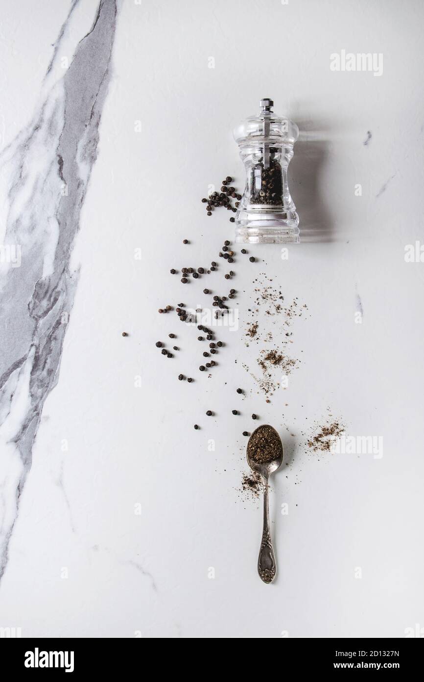 Schwarze Paprika Pfefferkörner und gemahlenes Pulver aus transparenter Pfeffermühle zu Löffel über weißem Marmor Textur Hintergrund. Draufsicht, Platz. Stockfoto
