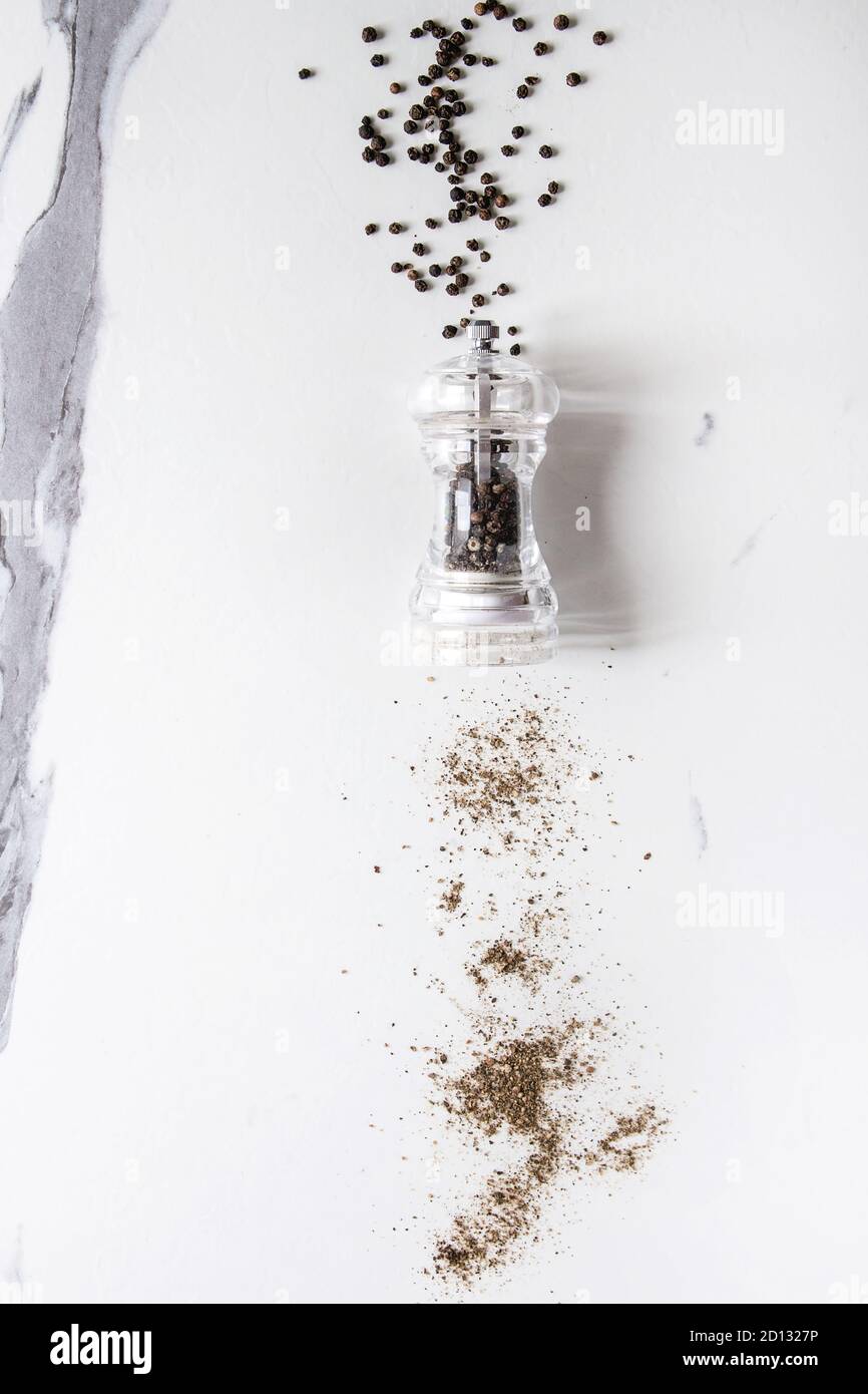 Schwarzer Pfeffer Pfefferkörner und Boden Pulver von transparent Pfeffer Mühle auf weißem Marmor Textur Hintergrund. Ansicht von oben, Platz. Stockfoto