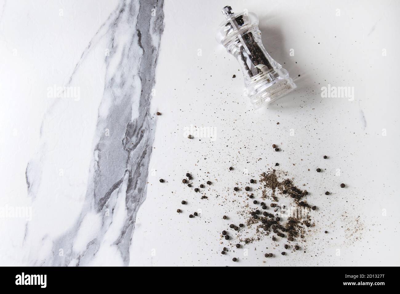 Schwarzer Pfeffer Pfefferkörner und Boden Pulver von transparent Pfeffer Mühle auf weißem Marmor Textur Hintergrund. Ansicht von oben, Platz. Stockfoto