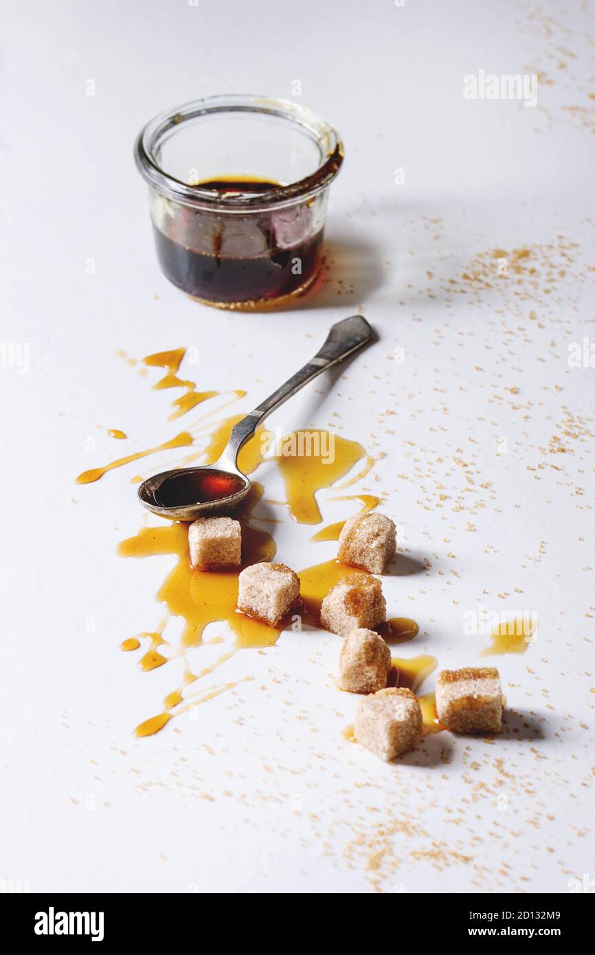 Hausgemachte Flüssigkeit transparent Brown Sugar caramel im Glas mit Löffel und Rohrzucker Würfel über weißem Marmor Hintergrund. Kopieren Sie Platz. Stockfoto