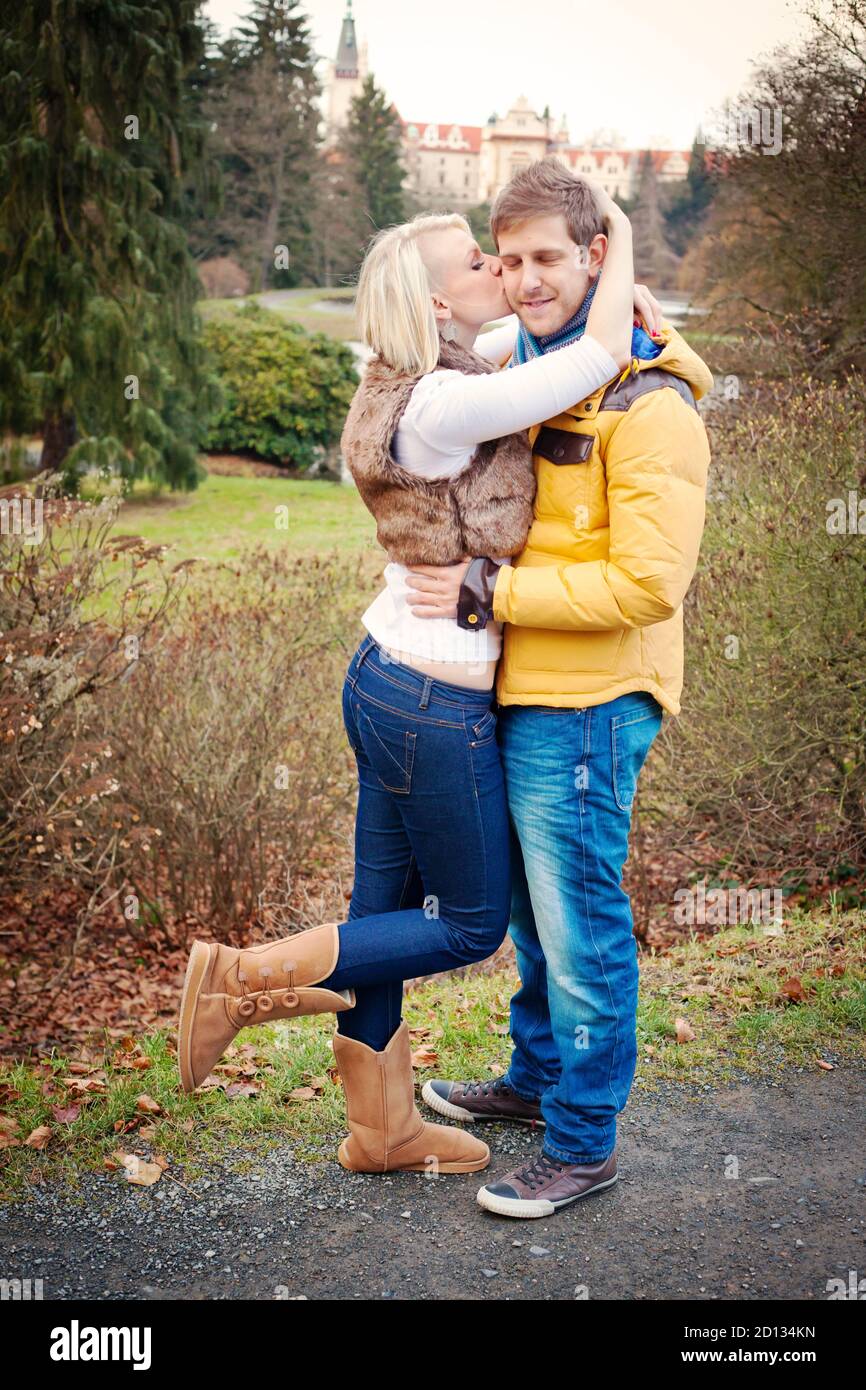 Glückliches Paar in einem Park. Die Frau küsst ihren Freund auf die Wange. Kaltes Wetter. Stockfoto