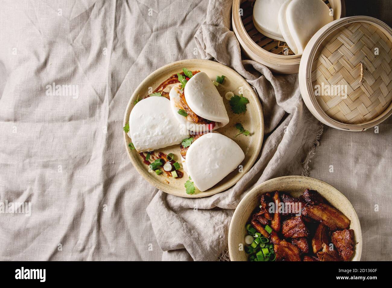 Asiatische sandwich gedämpft Gua bao Brötchen mit Schweinebauch, grünen und Gemüse in Keramik Teller über Bettwäsche Tischdecke. Im asiatischen Stil fast food Dinner Stockfoto