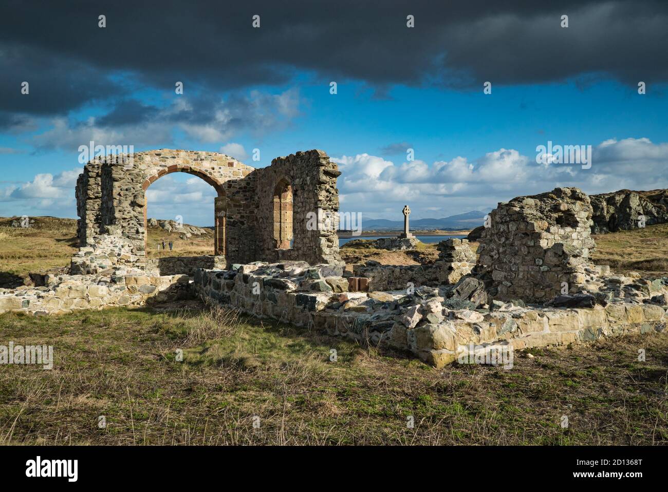 Dunkle Wolken hängen über den sonnenbeschienenen Ruinen der St. Dwynwen's Church auf der Halbinsel Llanddwyn, Anglesey Stockfoto