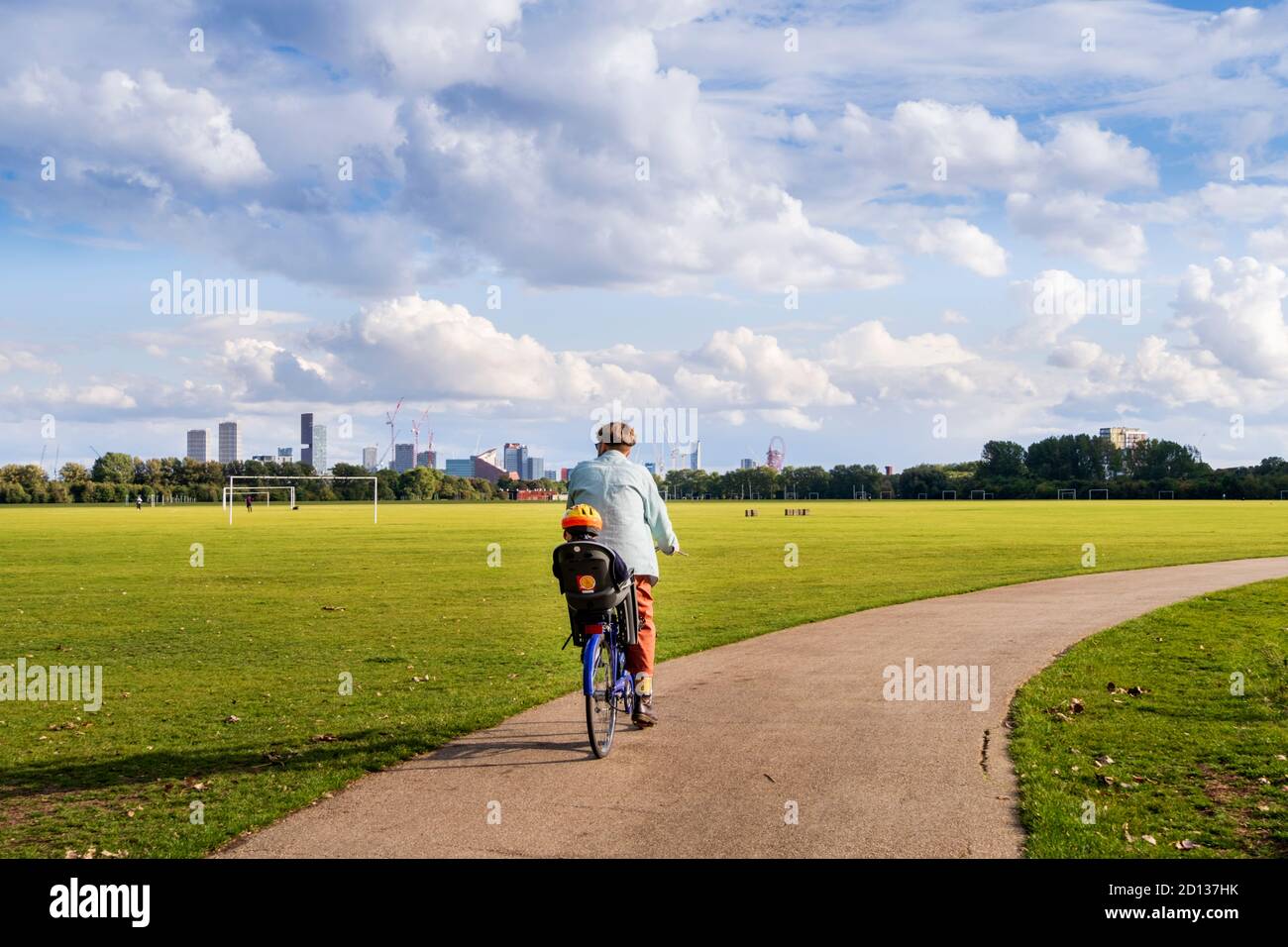 Großbritannien, London, Hackney Marshes. Ein Radfahrer mit einem Kleinkind in einem Sicherheitssitz auf einem Radweg in einem Londoner Park. Sonnig, Sommertag. Stockfoto