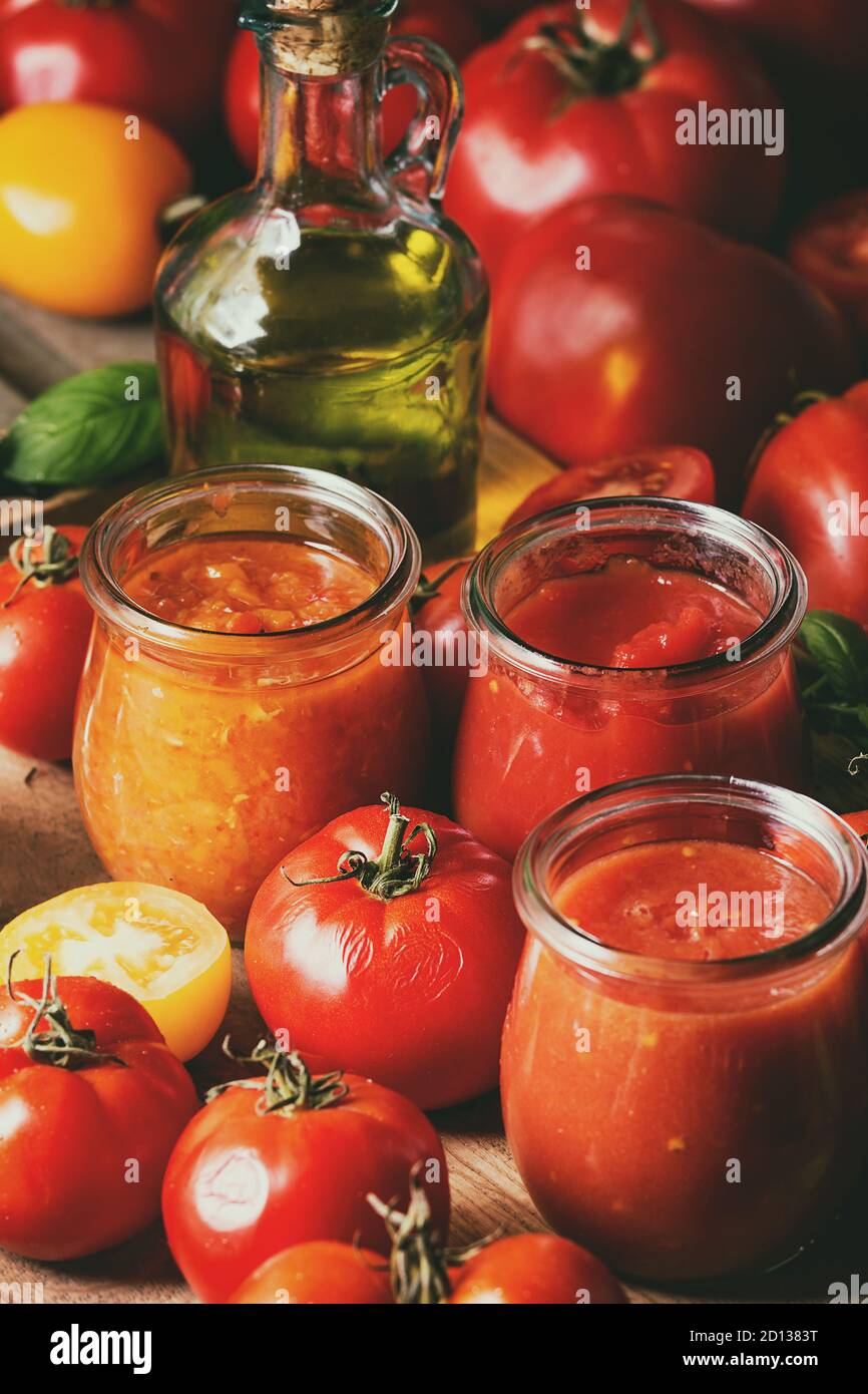Vielfalt von drei hausgemachten Tomatensaucen in Gläsern mit Zutaten oben. Verschiedene Arten von Tomaten, Basilikum, Olivenöl, Pfeffer, Salz. Nahaufnahme Stockfoto