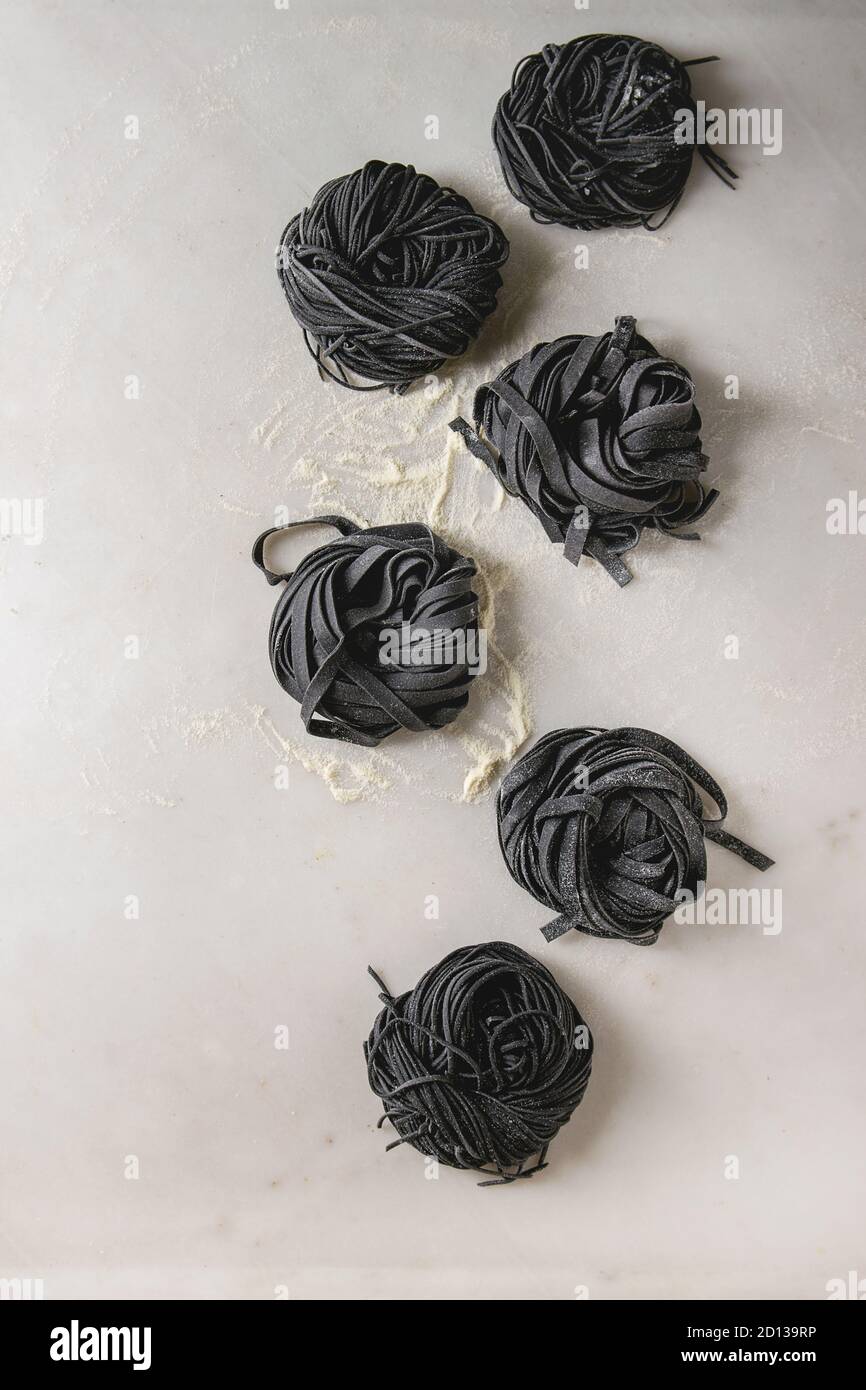 Vielzahl von italienischen hausgemachte Roh ungekocht Tintenfisch Tinte schwarz Pasta Spaghetti und Tagliatelle mit Grieß Mehl über weißem Marmor Hintergrund. Flat l Stockfoto
