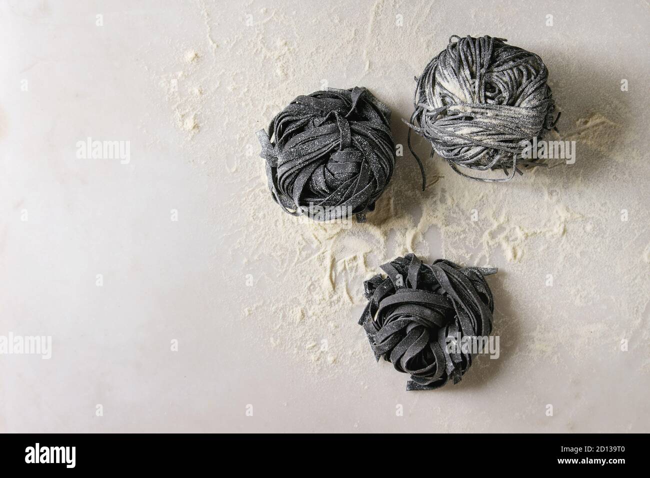 Vielzahl von italienischen hausgemachte Roh ungekocht Tintenfisch Tinte schwarz Pasta Spaghetti und Tagliatelle mit Grieß Mehl über weißem Marmor Hintergrund. Flat l Stockfoto