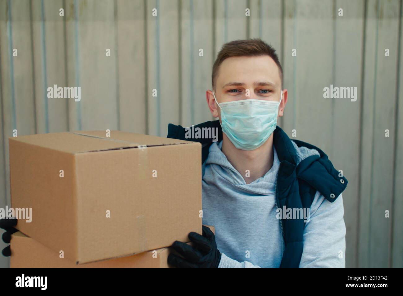 Happy Delivery Mann in einer Schutzmaske schaut auf die Kamera und hält zwei Boxen Stockfoto