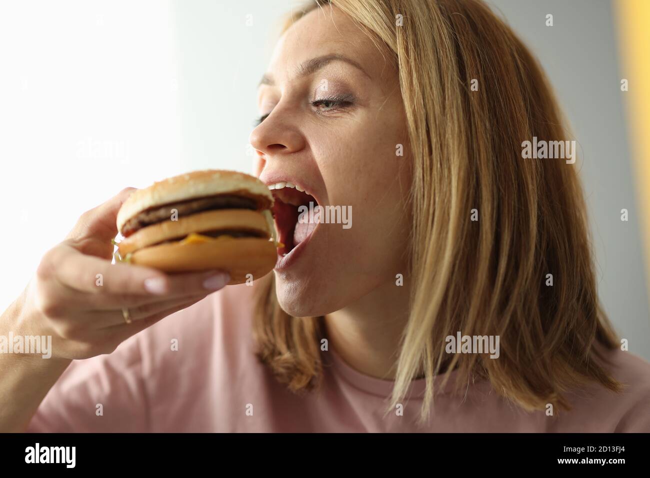 Junge Frau beißt ihr den weit geöffneten Hamburger in den Mund Stockfoto