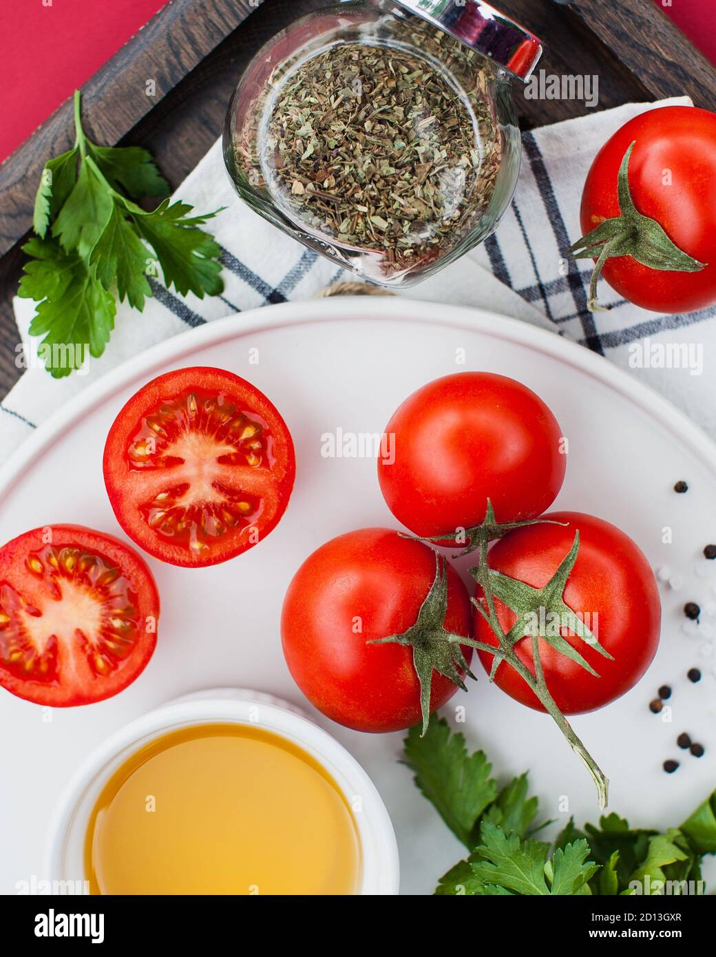 Reife rote Tomaten ganz auf einem Zweig und schneiden auf einem weißen Teller mit Gewürzen auf einem Holztablett. Foodfoto für ecomarket Stockfoto