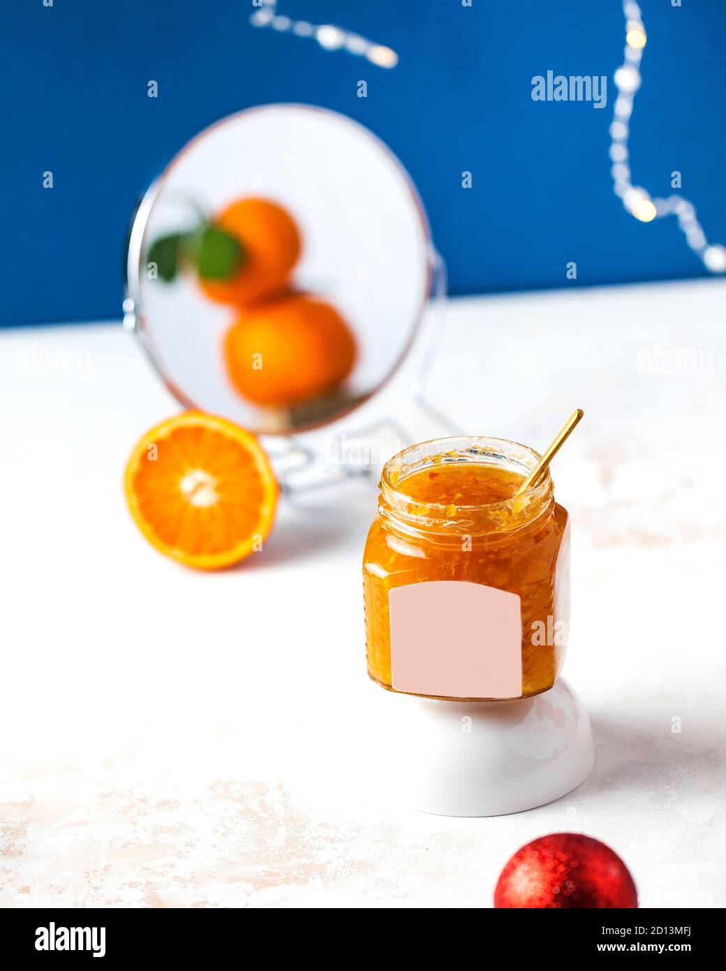 Mandarine Marmelade in einem Glas mit einem goldenen Löffel. Mandarinen werden in einem runden Spiegel reflektiert. Food-Foto. Stockfoto